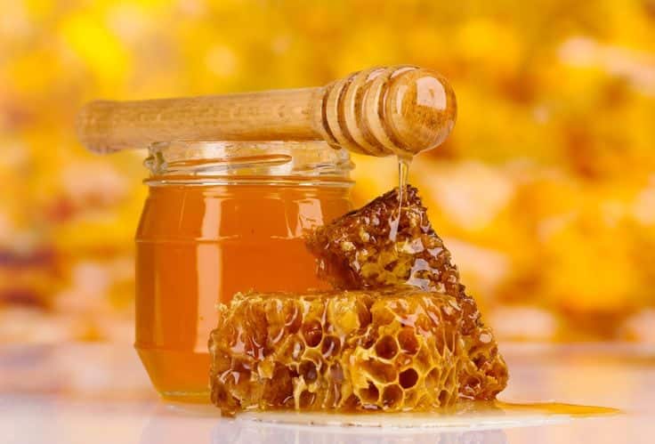 jar of honey, honeycombs and wooden drizzler on yellow background