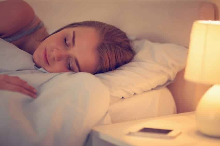 Brunette asleep next to smartphone with lamp on at home in bedroom