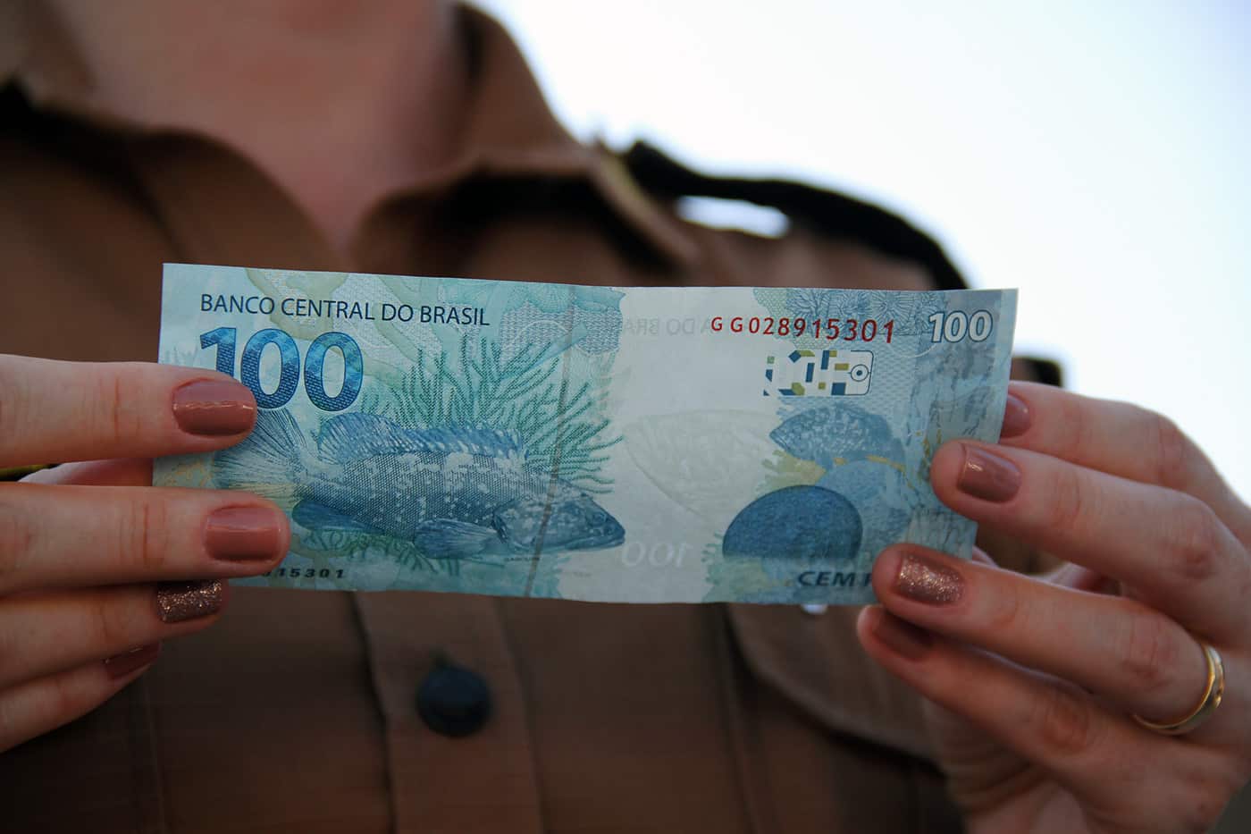 Fotografia de uma mulher segurando uma nota de 100 reais